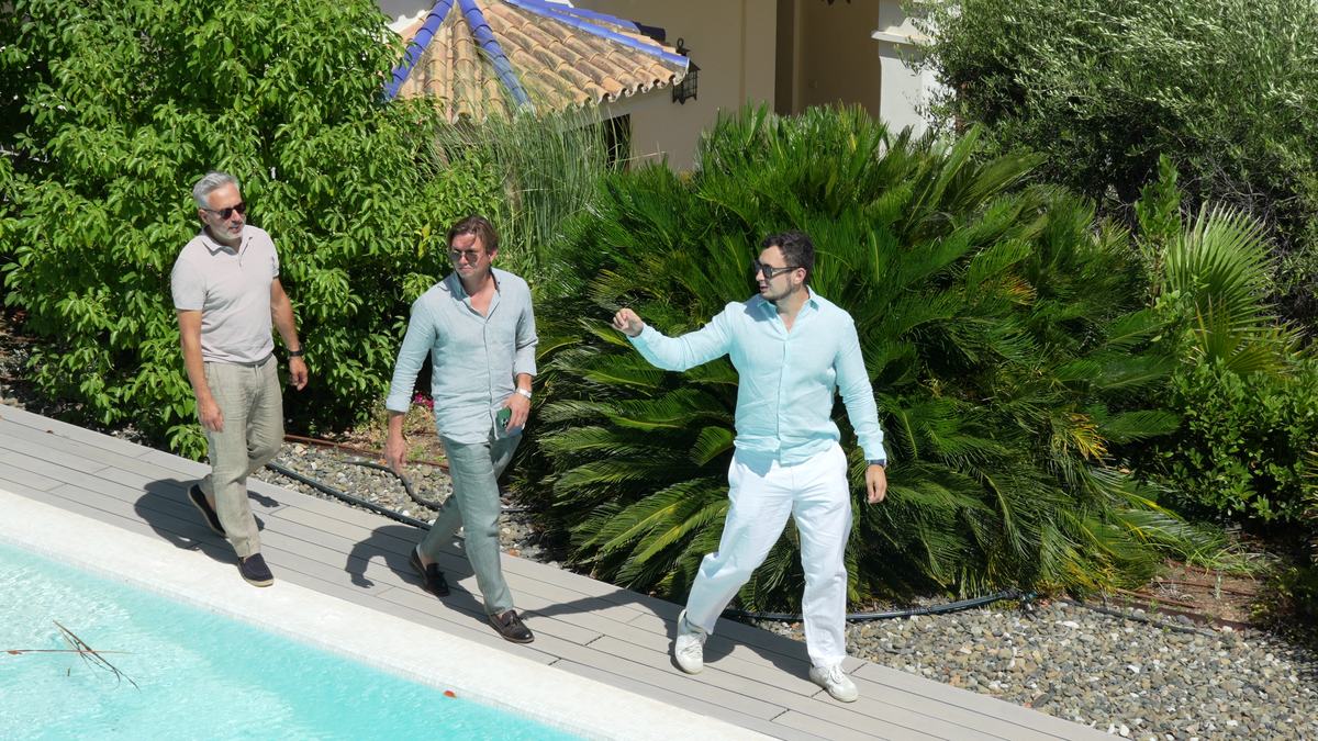 Three agents walking a client through a villa's poolside terrace