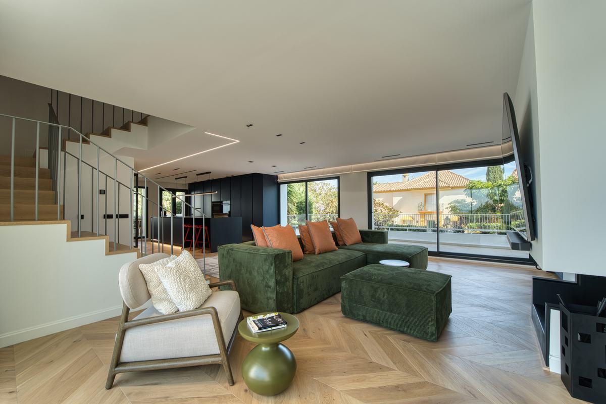 Living room with green sofa, herringbone floor and open staircase